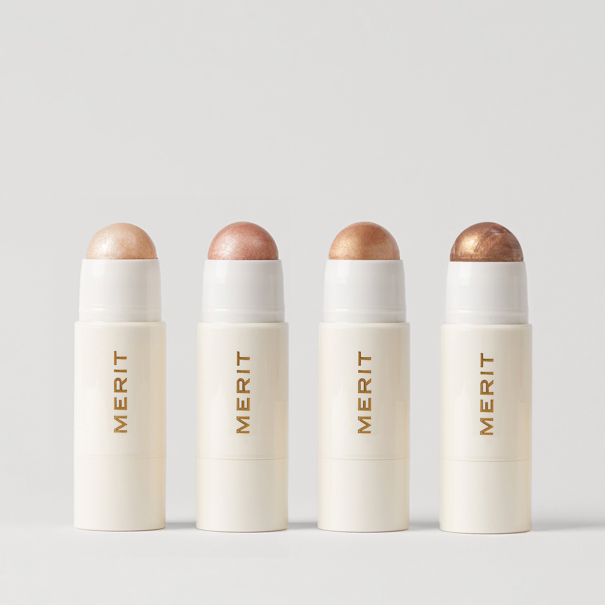 Master ||  Four stick highlighters with the brand name MERIT written on it, with the product cap removed, revealing the highlighter balm