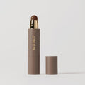Master || A stick complexion product with MERIT written on it, with the cap removed, showing the product in shade Umber.