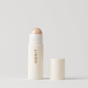 Master ||  A stick highlighter with the brand name MERIT written on it, with the product cap removed, revealing the highlighter balm.